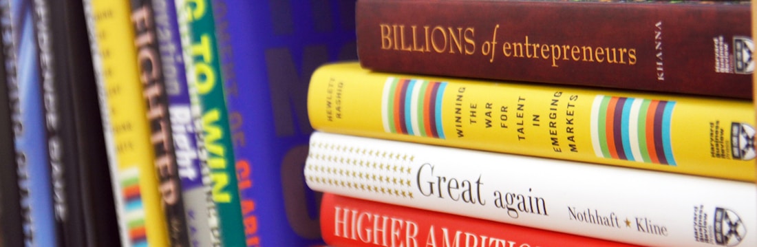 A collection of business and motivational books on a shelf, featuring titles like 'Greening Your Business,' 'Billions of Entrepreneurs,' 'Great Again,' and 'Higher Ambition.' The books are arranged vertically, showing a variety of colors and sizes.